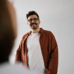 A cheerful man wearing glasses and a casual shirt standing indoors, captured naturally.