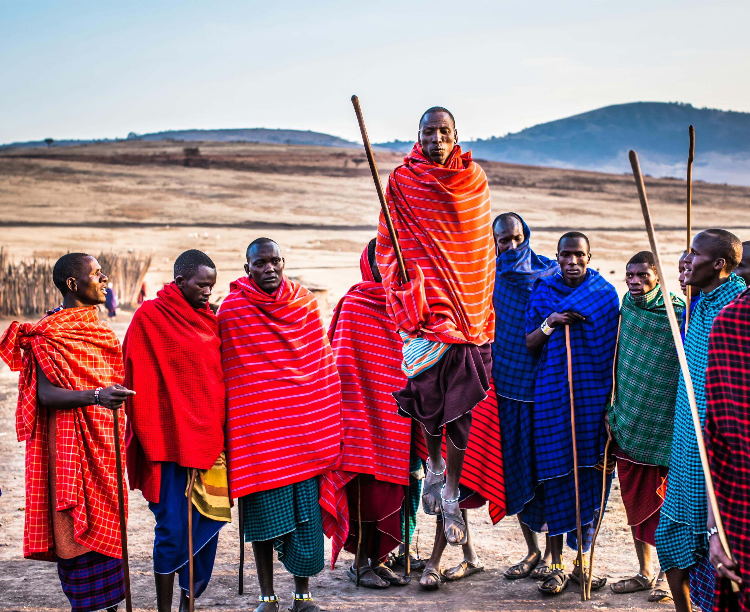 A group of Maasai men in vibrant traditional attire performing a cultural jumping dance outdoors.