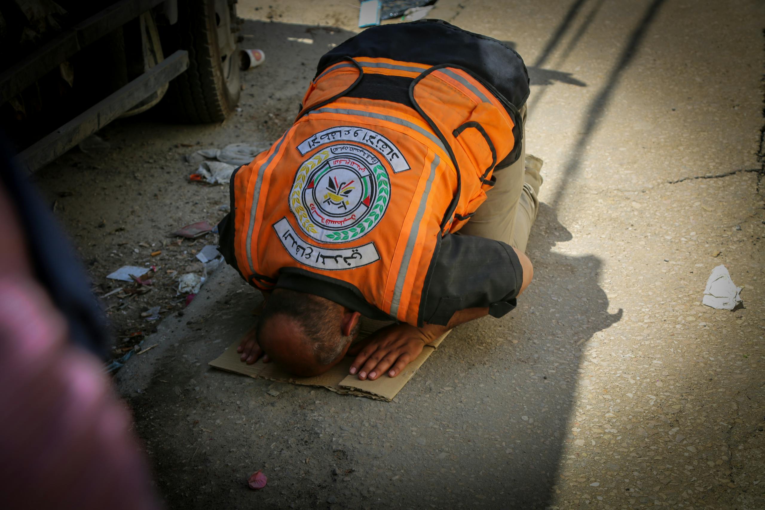 An emergency worker in an orange vest prays on a street in Gaza, depicting a moment of faith amidst turmoil.