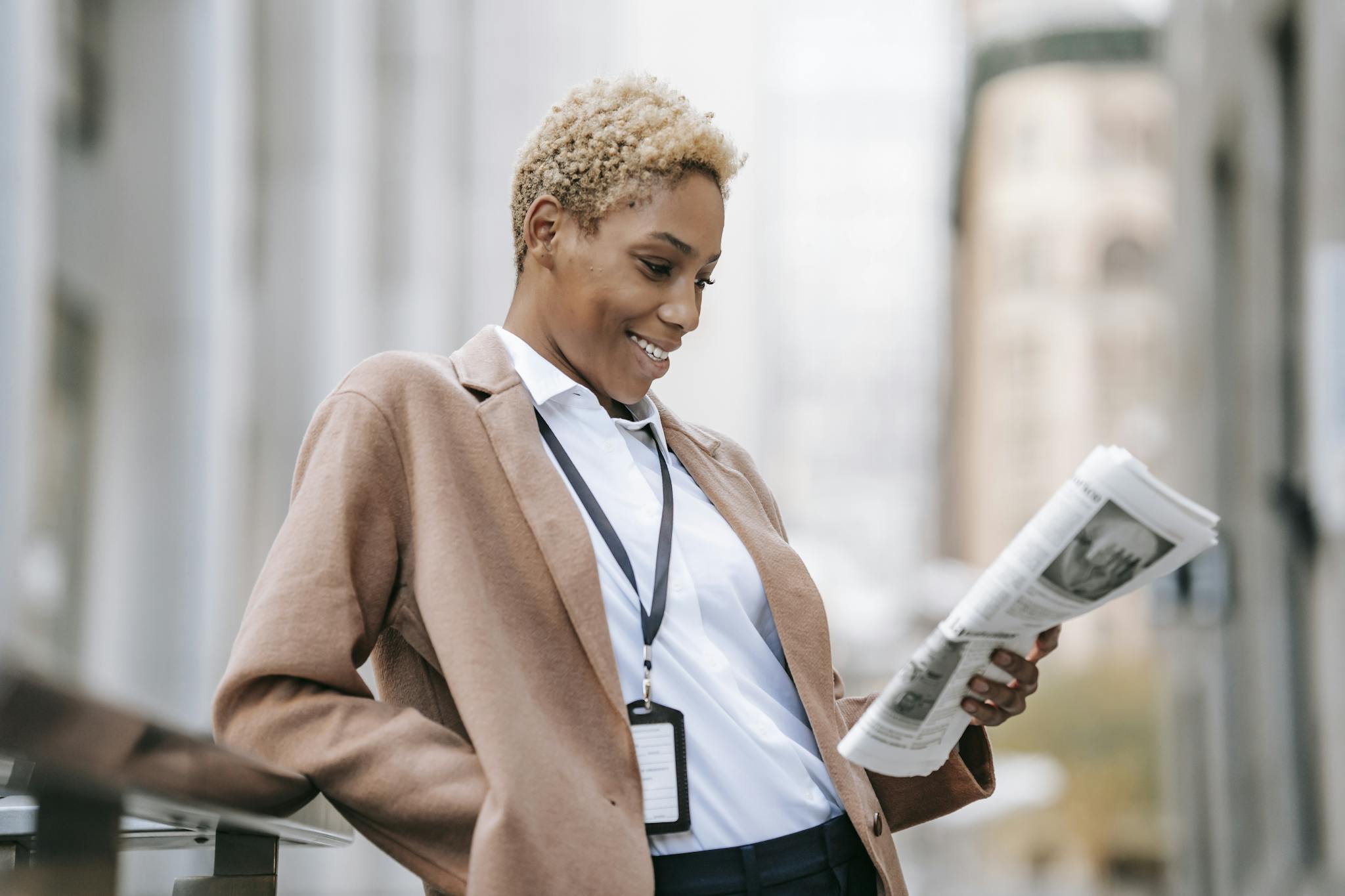 Confident businesswoman smiling while reading a newspaper outdoors in an urban setting.