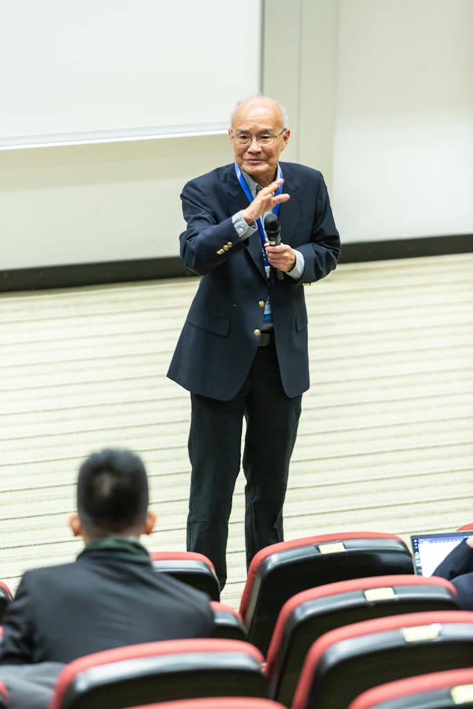 Elderly man delivering a speech in a lecture hall, engaging audience.