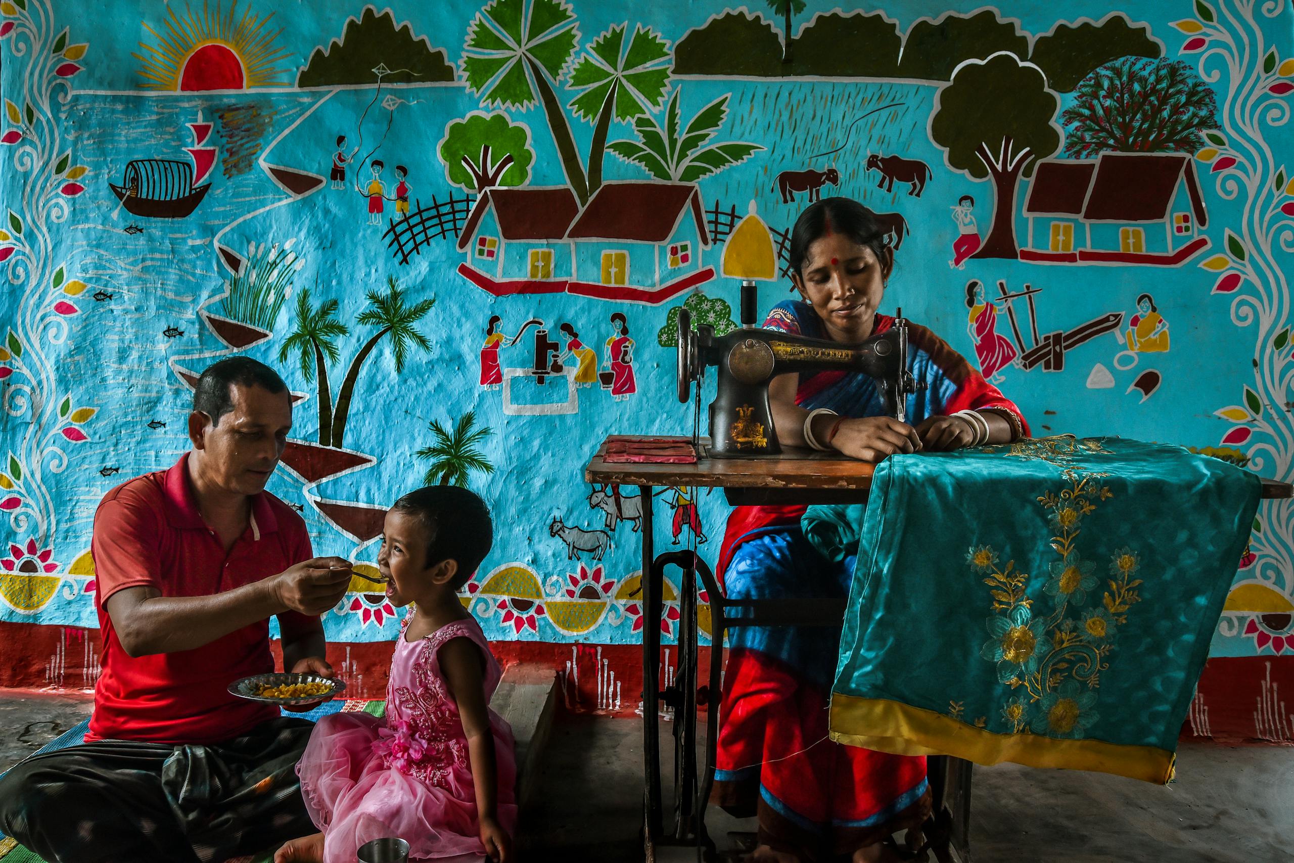 Family scene with sewing and feeding at home in Rajshahi, Bangladesh.