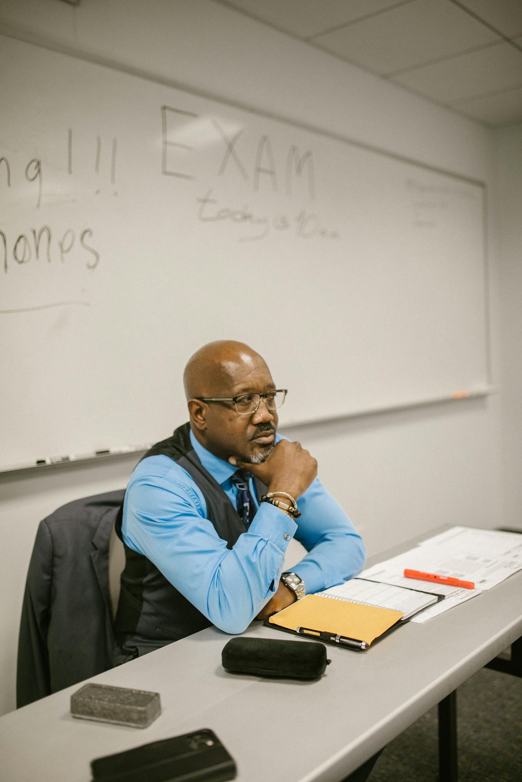 Mature teacher sitting at desk proctoring an examination in a classroom.
