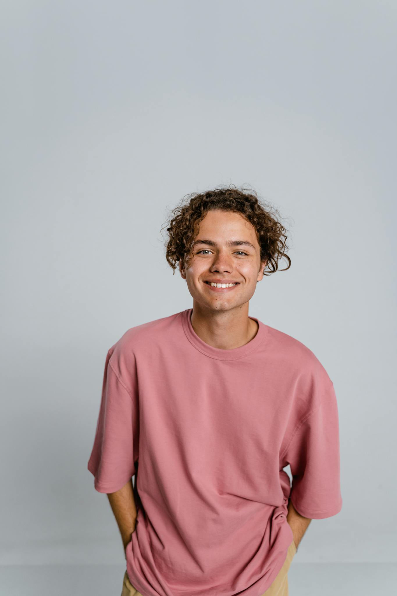 Portrait of a cheerful young man wearing a pink t-shirt, smiling directly at the camera in a studio setting.