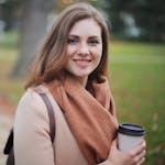Portrait of a smiling woman holding a coffee cup in a serene autumn park setting.