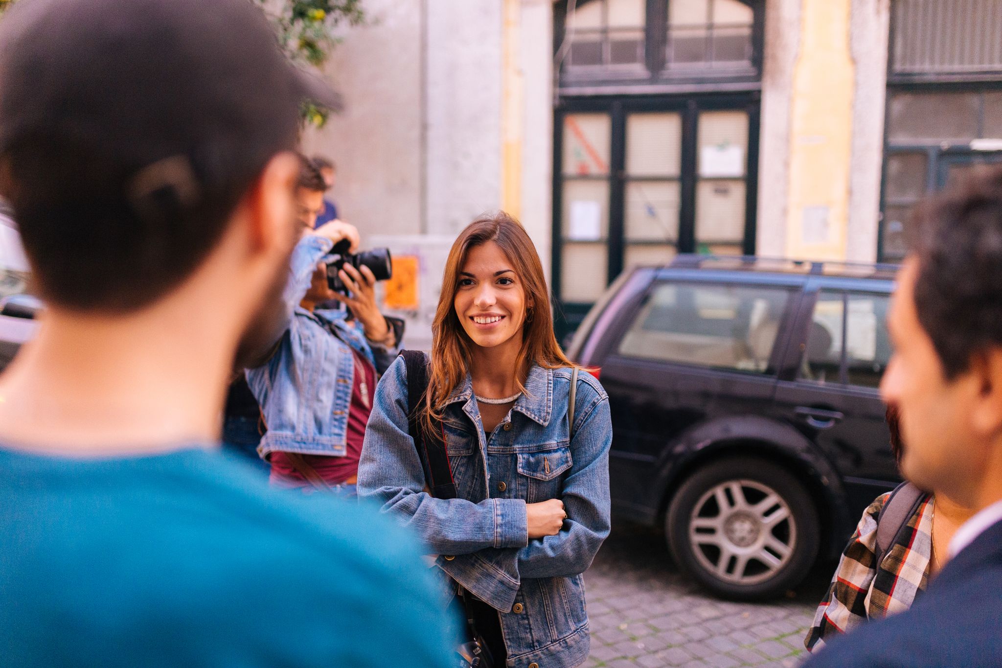 A group of friends smiling and interacting on a city street during the day.